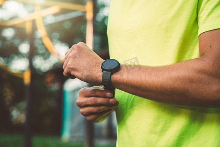 运动手表摄影照片_穿着绿色衬衫的健康男人在跑步时戴着运动手表