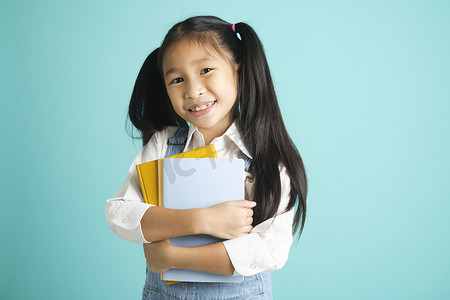 孩子上学摄影照片_特写孩子学生女孩微笑着拿着书，去上学。