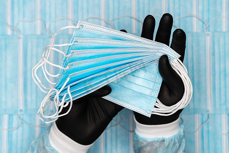 医务人员手里拿着许多戴着黑色防护手套的蓝色外科口罩。