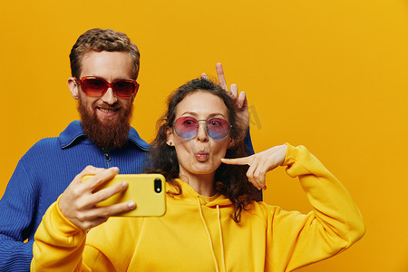 生活搞笑摄影照片_在黄色背景下，女人和男人带着手机的搞笑情侣手握社交网络和歪歪扭扭的交流自拍微笑很有趣。