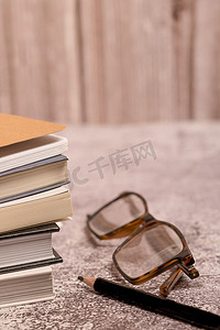 一副眼镜和一支黑色铅笔的一堆书