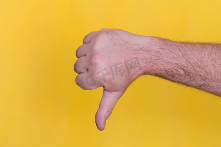 拳头指向摄影照片_黄色背景上的拇指向下标志