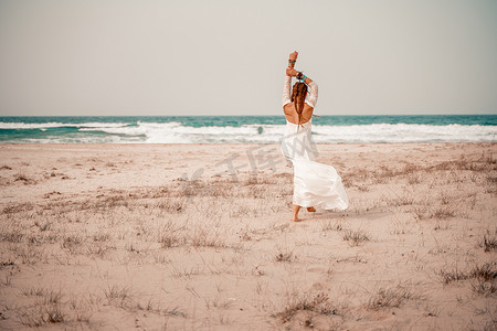 沙滩上的模特摄影照片_在沙滩上穿着白色长裙和银首饰的波西米亚风格模特。