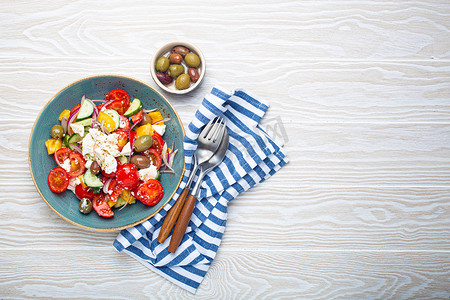纯白色模板摄影照片_白色木质背景中蓝色碗中的希腊沙拉，配有菲塔奶酪、蔬菜和橄榄