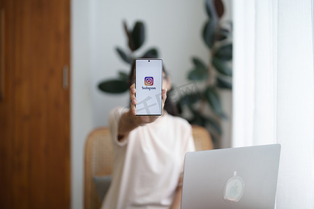 泰国清迈 - 2022 年 7 月 9 日：一位女士在咖啡馆的屏幕上拿着带有 Instagram 应用程序的智能安卓手机。