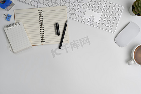 空白记事本、咖啡杯、无线耳机和白色桌子上的鼠标的顶部视图。