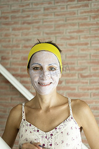 放松的女人在脸上涂矿物粘土面膜以恢复活力，头上有头带