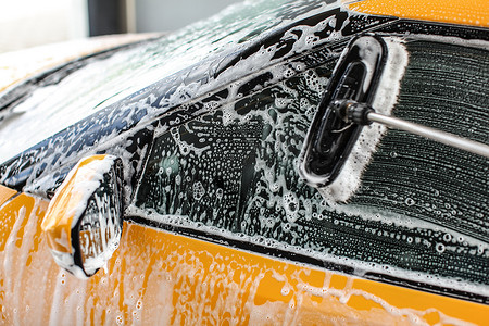 流动汽车摄影照片_在自助洗车中清洗的黄色汽车侧窗。