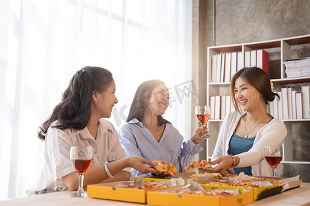 一群亚洲朋友聚在一起，喝着香槟，在家吃披萨庆祝圣诞节。