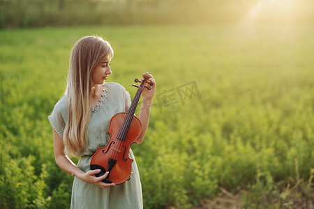 拿小提琴摄影照片_夕阳下，女音乐家小提琴手手里拿着小提琴
