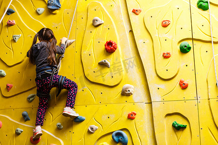 女孩攀岩摄影照片_上升在室外攀岩健身房的小女孩