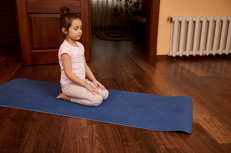 练习瑜伽时，可爱的小女孩闭着眼睛在健身垫上冥想