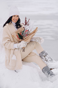 一个穿着米色开衫、开着冬花的女孩正坐在白雪皑皑的公园里的大自然中。