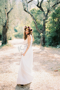 身穿白色连衣裙、头戴花环的微笑新娘站在公园里