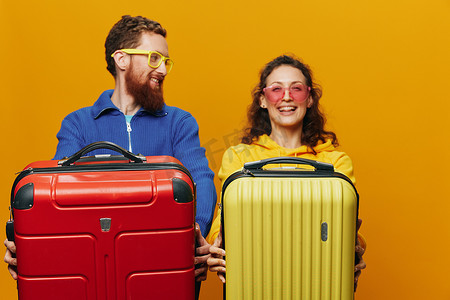 广告黄色摄影照片_女人和男人微笑着，手里拿着手提箱，黄色和红色的手提箱愉快地微笑着，弯曲着，黄色背景，去旅行，家庭度假旅行，新婚夫妇。