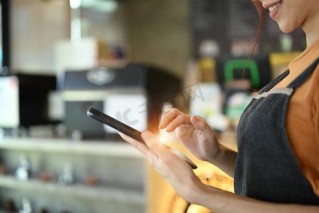企业家剪影摄影照片_站在现代咖啡馆柜台前，穿着围裙、使用数字平板电脑微笑的女企业家的剪影