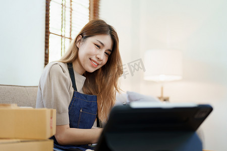独立的年轻亚洲女性在线卖家的小企业创业者正在使用智能手机并接受订单来包装产品以交付给客户。