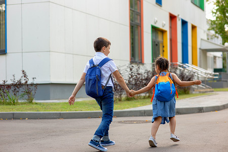 男孩衬衫摄影照片_一个小女孩和一个男孩穿着白衬衫背着背包跑在上学的路上。