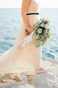 新娘海边摄影照片_新娘手中的花束在石滩上