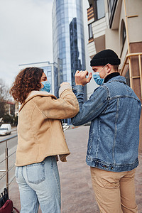 一对戴着防护面具的夫妇在检疫时间在商业大楼附近的城市互相问候。