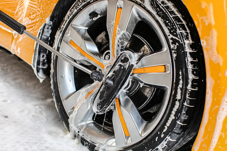洗车请左转谢谢摄影照片_在自助洗车中清洗的黄色车轮，用洗发水覆盖的刷子清洁铝轮辋盘