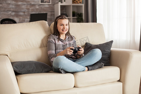 孩子电子游戏摄影照片_戴牙套的小女孩坐在沙发上玩电子游戏