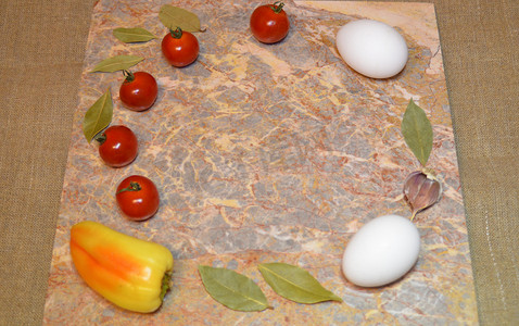 大理石表面上的蔬菜和两个白鸡蛋，有自由空间：樱桃番茄、甜椒、大蒜和月桂叶