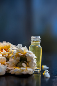 小玻璃瓶中雏菊精华或浓度的特写镜头，以及一些新鲜的雏菊或英国雏菊花，黑板上背景模糊，瓶子上有边缘光。