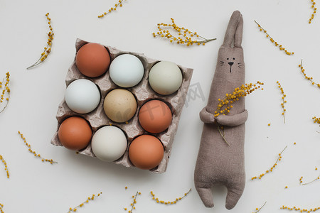 兔子黄色摄影照片_有趣的手工兔子玩具，配有彩色鸡蛋和黄色含羞草花。