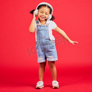 在孤立的红色背景下，戴着音乐耳机、有趣的收音机或儿童播客跳舞、精力充沛或小女孩。