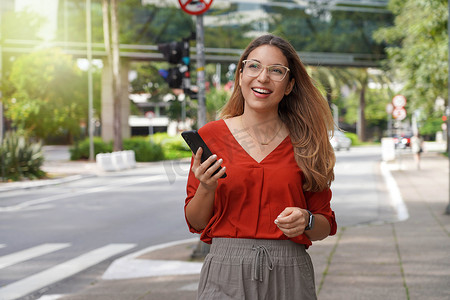 拿着手机的微笑的女商人走在现代能承受的大都市