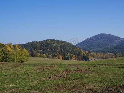 luzicke lusitian hory 山日落景观前的绿色草地，秋季色彩缤纷的森林和树木和山丘
