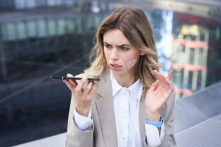 莫生气摄影照片_女人在手机上留言时看起来很生气，皱着眉头对着扬声器说话