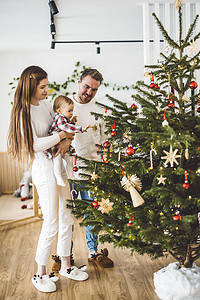 家庭树摄影照片_装饰圣诞树的年轻白人家庭垂直全家福