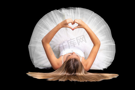 身穿白色裙子的芭蕾舞女演员躺在地上，双手展示一颗心，黑色背景中的肖像