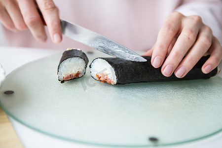 制作寿司的过程，女孩制作不同口味的寿司——新鲜的三文鱼、鱼子酱、牛油果、黄瓜、生姜、米饭。