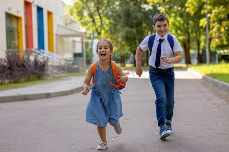跑了摄影照片_快乐的小学生，一​​个穿着白衬衫背着背包的男孩和女孩，从学校跑了出来。