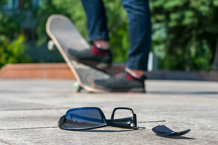 丢失的黑眼镜躺在路上，背景是一名男子在滑板上滑冰