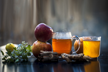 苹果草药和有机汁与橙汁、肉桂棒、柠檬汁、生姜或阿德拉克以及一些图尔西叶或圣罗勒叶的特写镜头，放在透明玻璃杯中，包含所有原料。