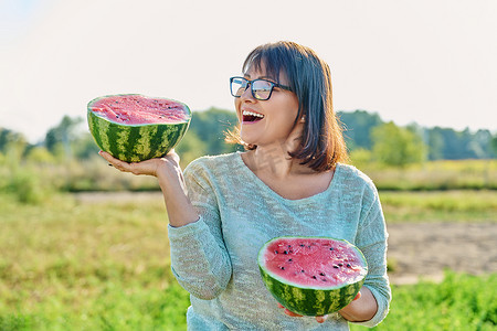 西瓜采摘摄影照片_微笑的女人手里拿着半个成熟的西瓜，户外