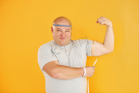 胖运动摄影照片_黄色背景中戴着运动头带的风趣超重男人
