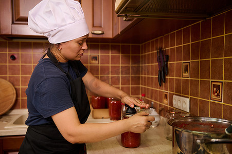家庭主妇用罐装新鲜煮沸的番茄汁或帕萨塔罐头盖上盖子，用封口机或特殊封口键