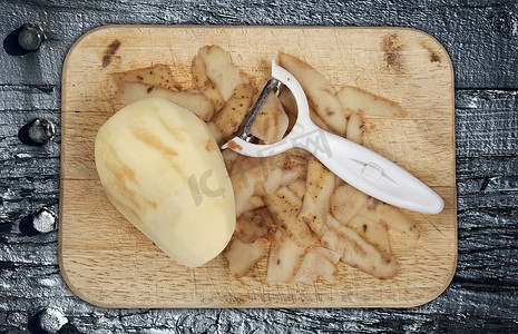 生土豆在木砧板上去皮，木砧板上有削皮器