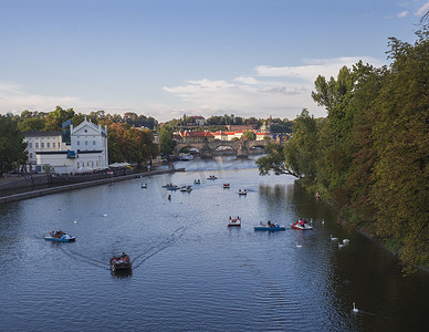 伏尔塔瓦河上的查理大桥全景和捷克共和国布拉格老城区的房屋，黄金时段的灯光，夏日阳光明媚的日子，游客在脚踏船上放松