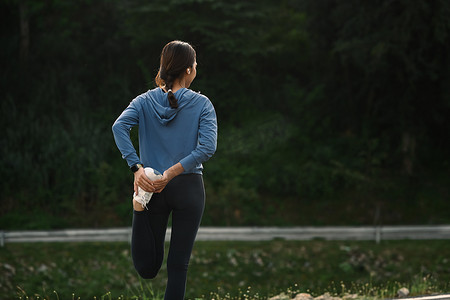 跑步运动的人摄影照片_在公园跑步前伸展运动的女人的背影。