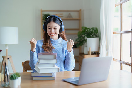 学习材料摄影照片_年轻美丽的亚洲女性在清晨在线课堂上以书籍、耳机和电脑作为家里的学习材料时露出笑脸的肖像