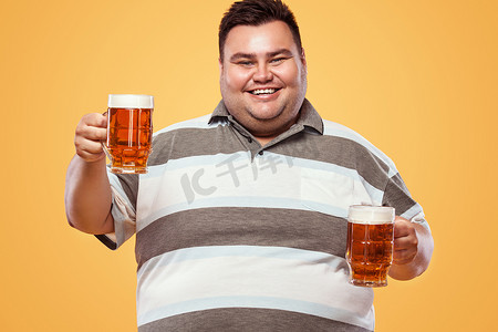 慕尼黑十月啤酒节摄影照片_慕尼黑啤酒节上的年轻胖子，在黄色背景下喝啤酒。