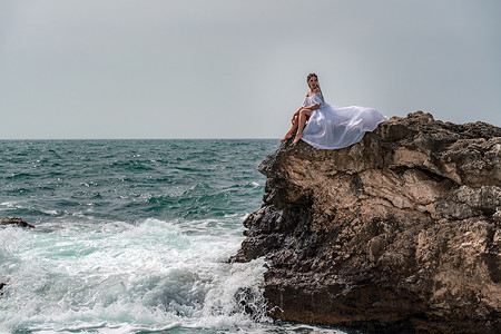 海中石头摄影照片_暴风雨中的女人坐在海中的一块石头上。