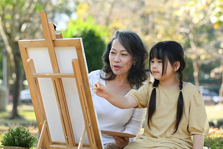 可爱的小女孩和祖母在夏日公园画画，一起在户外度过休闲周末