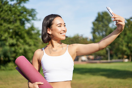 运动健身女孩在公园用橡胶瑜伽垫自拍，锻炼并在社交媒体上分享照片